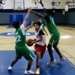 Youth basketball game with intense defense on a shot attempt.