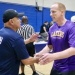 Two men shaking hands on a basketball court, one in Lakers shirt.