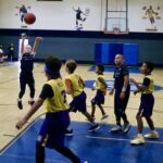 Kids playing basketball in a gym with a player shooting the ball.