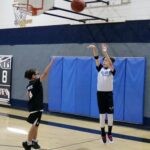 Two boys playing basketball, one shooting and the other defending.