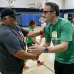 Two men warmly greeting each other in a gymnasium.