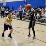 Two young boys playing basketball in a gymnasium during a game.
