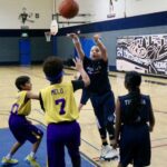 Kids playing basketball indoors, one shooting a basket.