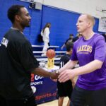 Two men exchanging a basketball trophy in a gym.