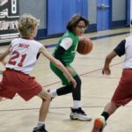 Youth basketball game with a player dribbling between defenders.