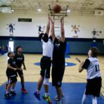 Two boys jumping to grab a basketball during a game in a gym.