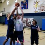 Boys playing basketball indoors, one attempting a shot.