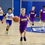 Young kids playing basketball indoors, with one boy dribbling the ball.