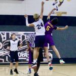Two basketball players jump to reach the ball during a game.