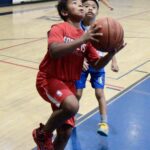 Young boy in red jumps to score a basketball point indoors.