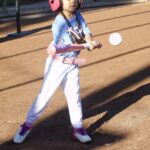 Young girl playing baseball, mid-swing.
