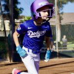 A young baseball player in a Dodgers uniform running on the field.