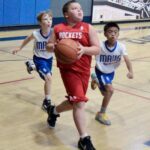 Young basketball player in red drives past defenders.