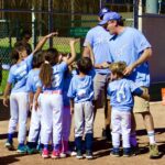 Youth baseball team huddling with coaches on the field.