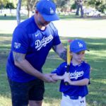 Father and son in Dodgers gear at a park, sharing a moment.