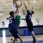 Three boys playing basketball indoors during a jump shot.
