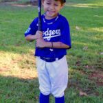 A young boy in a Dodgers baseball uniform holding a bat on a grassy field.