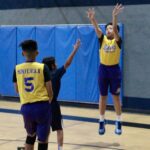 A basketball player jumps to shoot while a defender raises an arm to block.