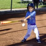 Young child in a blue baseball uniform swinging a bat at a ball.