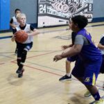 Young basketball player dribbles past defenders in a gym game.
