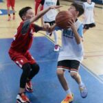 Young boys playing basketball, one attempting to block the other.