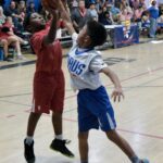 Two youth basketball players competing for a rebound in a gymnasium.