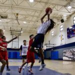 A basketball player leaps for a shot while defenders try to block him.