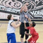 Referee tossing the basketball for a tip-off between two young players.