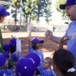 Coach giving a thumbs-up to young baseball players in purple caps.