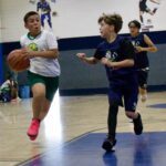 Two boys playing basketball indoors, one dribbling the ball.