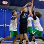 Three boys playing basketball indoors, reaching for the ball.