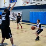 Young basketball players practicing shooting and defense in a gym.