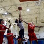 Young basketball player jumps to shoot as defenders try to block.