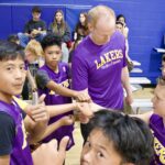 Basketball coach motivating young players wearing Lakers shirts during a game.