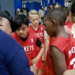 Youth basketball team in red jerseys gathered around coach.