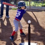 Young child batting in tee-ball practice under sunlight.