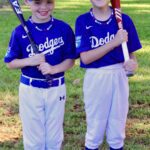 Two young baseball players in Dodgers uniforms holding bats outdoors.