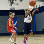 Two boys playing basketball indoors, one shooting the ball.