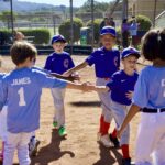 Children in baseball uniforms high-fiving after a game.