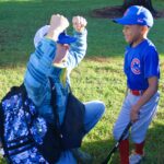 Child cheering for young baseball player in uniform.
