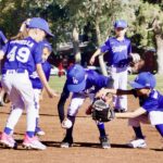 Young baseball players in blue uniforms playing on a sunny field.