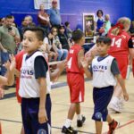 Young basketball players on the court during a game with spectators in the background.