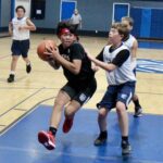 Two boys competing in a basketball game inside a gymnasium.