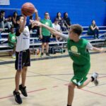 Youth basketball player shooting over a defender in a gym.