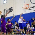 Youth basketball game action with a player shooting and defenders attempting to block.