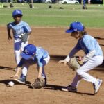 Young baseball players fielding a ground ball during practice.