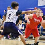Two boys playing basketball, one in red and one in white jersey.
