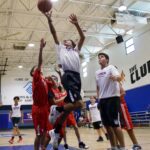Teen basketball players compete intensely in a gym during a game.