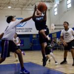 A female basketball player jumps to shoot while opponents defend.