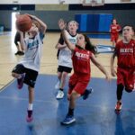 Young girls playing basketball in a gymnasium.